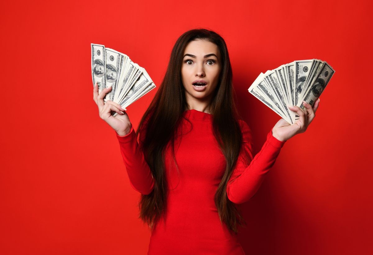 portrait of a cute, tender, attractive, gorgeous girl in a red dress, holding two fans at 100 dollars, won by a gorgeous lady. isolated over bright red background